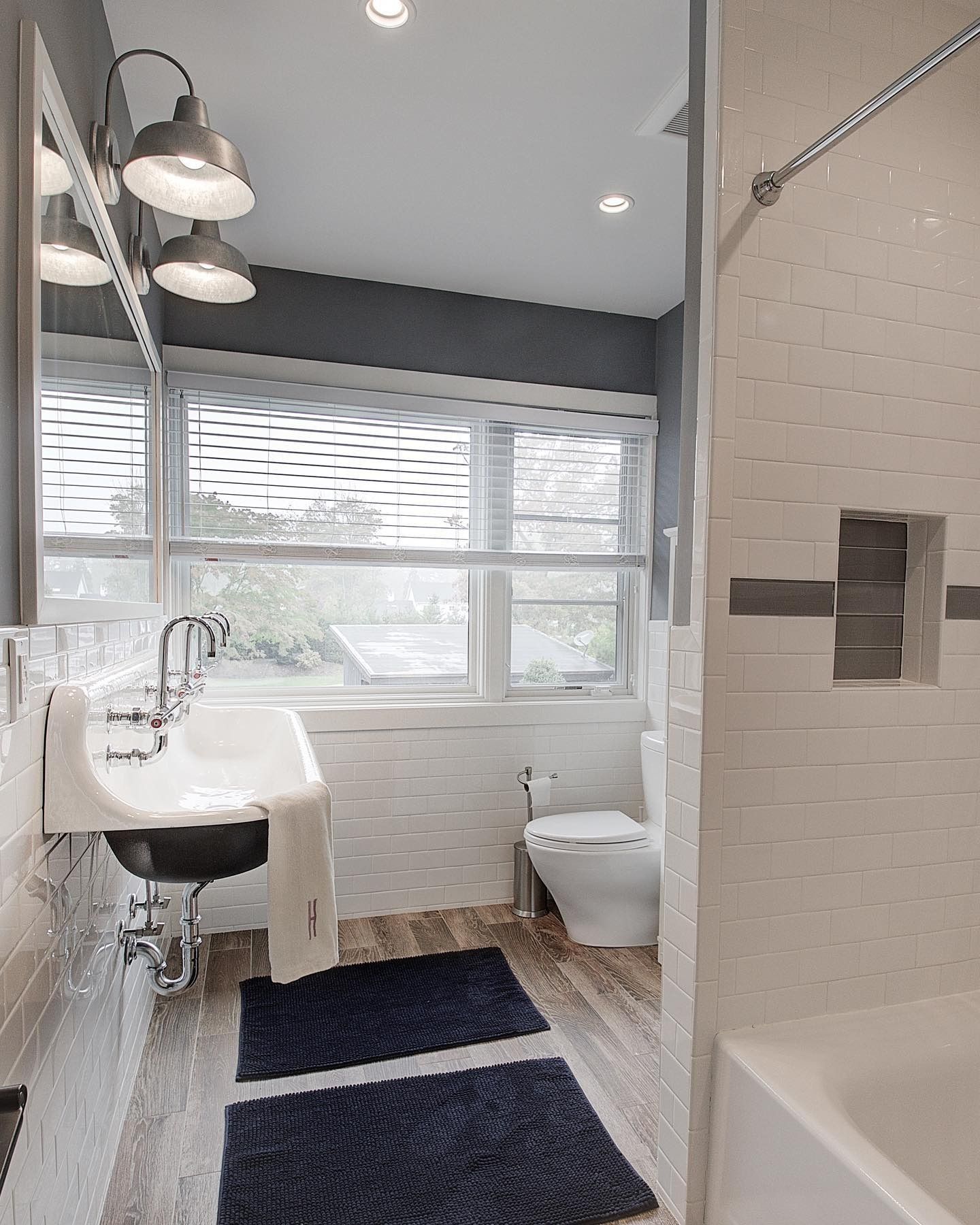Bathroom with white tile, a window, a white sink, and blue rugs.