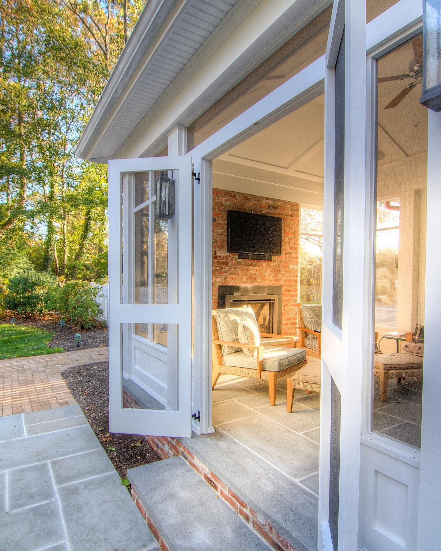 White French doors open to a sunroom with a brick fireplace, TV, and armchairs.