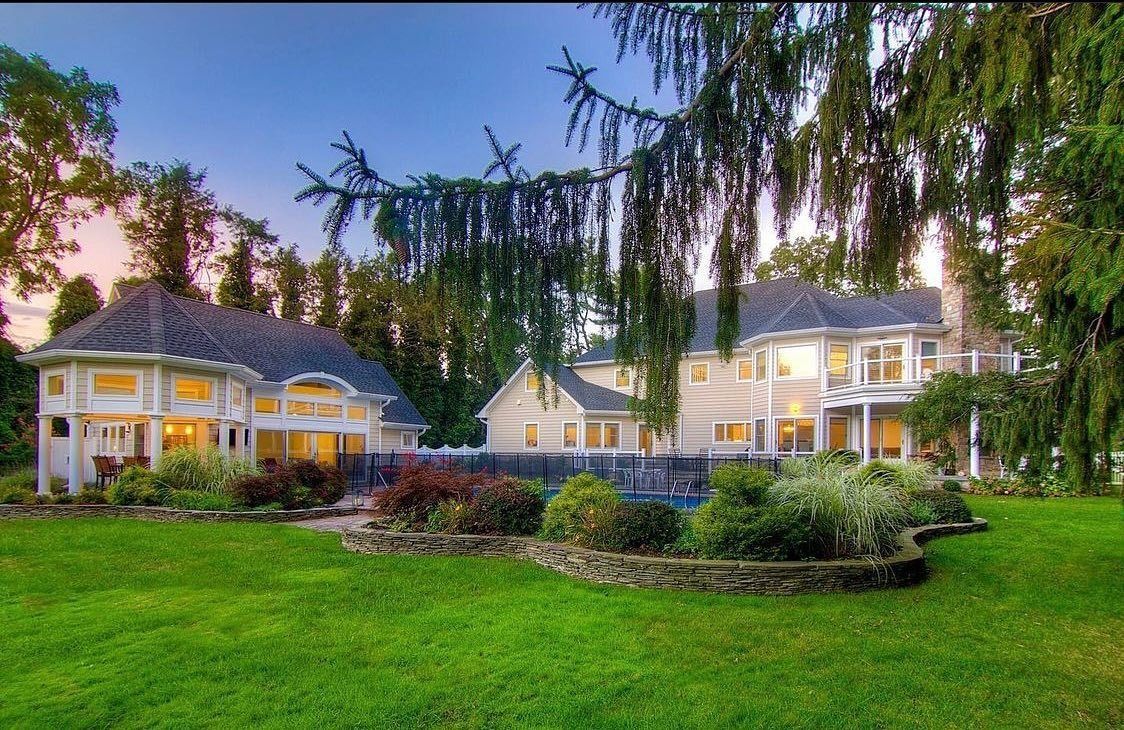Large house with lush green lawn, trees, and gardens. A swimming pool is visible.