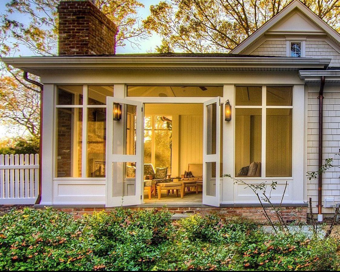 Screened porch with white trim, brick chimney, and open double doors. Sunlight streams into the interior.