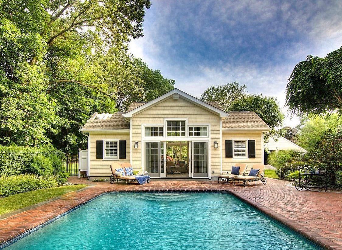 Yellow house with pool, surrounded by trees. Two lounge chairs near a doorway.