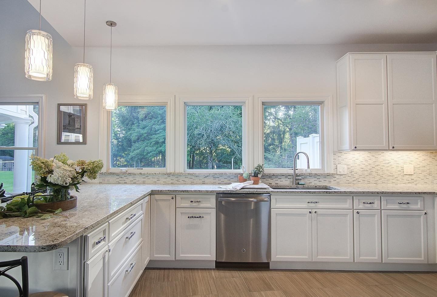 White kitchen with granite countertops, stainless steel appliances, and windows overlooking greenery.