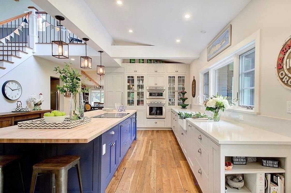 Spacious kitchen with blue island, white cabinets, wood floors, and natural light from windows.