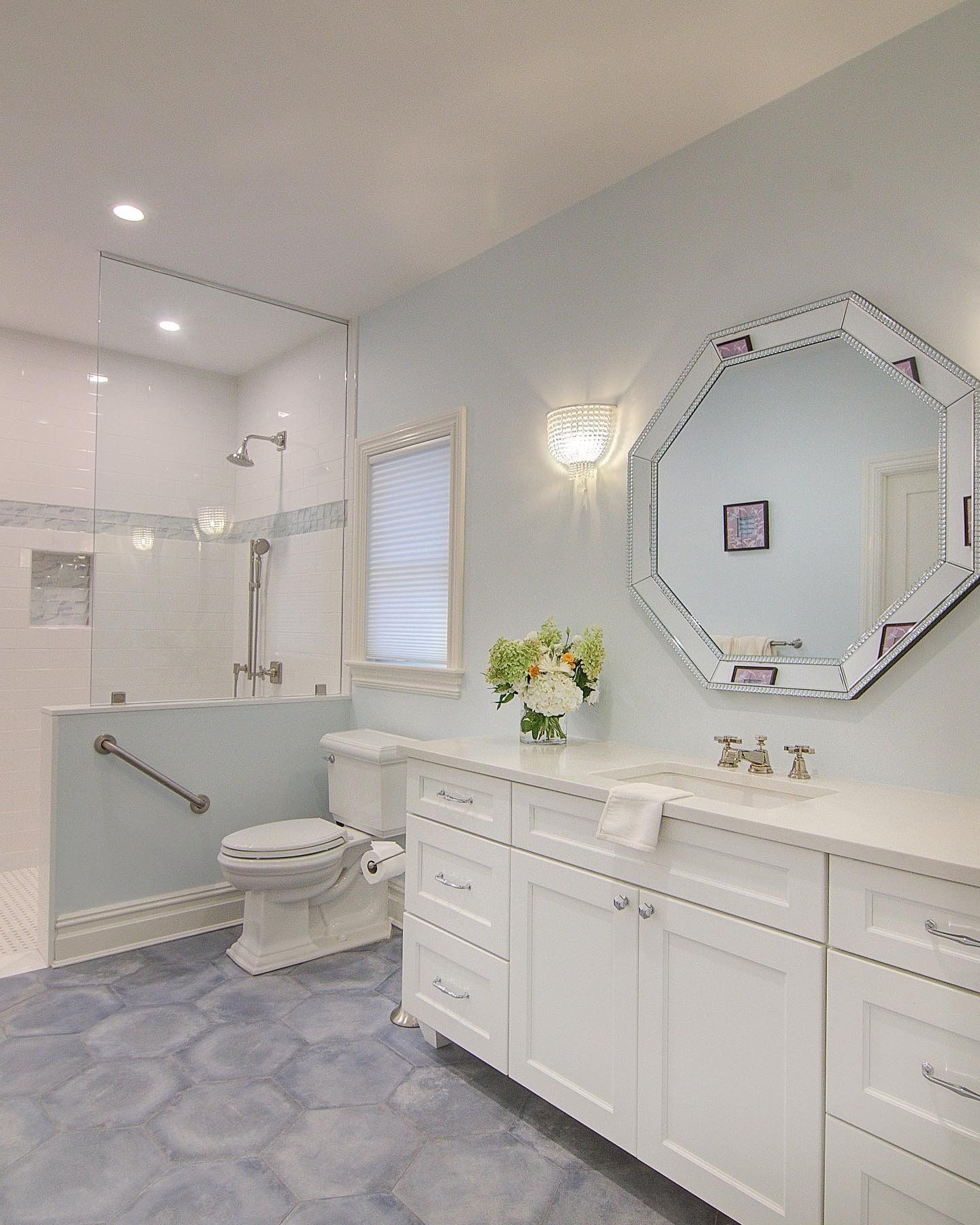 Bathroom with blue hexagonal tile floor, white vanity, and octagonal mirror. Shower with glass enclosure.