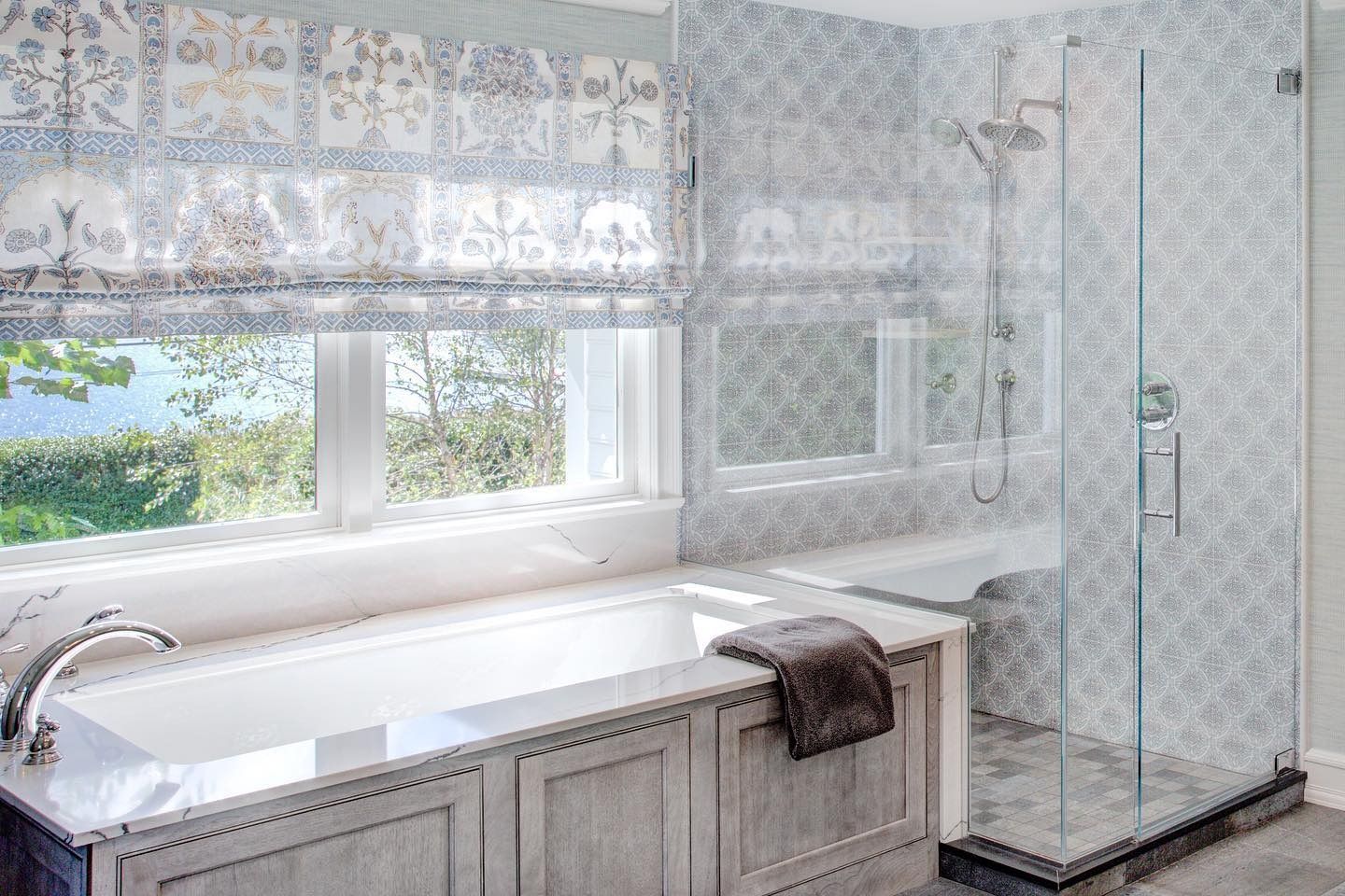 Bathroom with floral patterned tile, tub, and glass shower. Window with floral blind and scenic view.