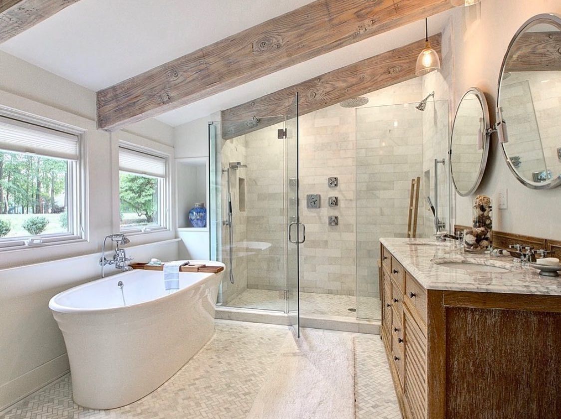 Luxury bathroom with freestanding tub, glass shower, and wooden vanity. Features stone tile and exposed wood beams.
