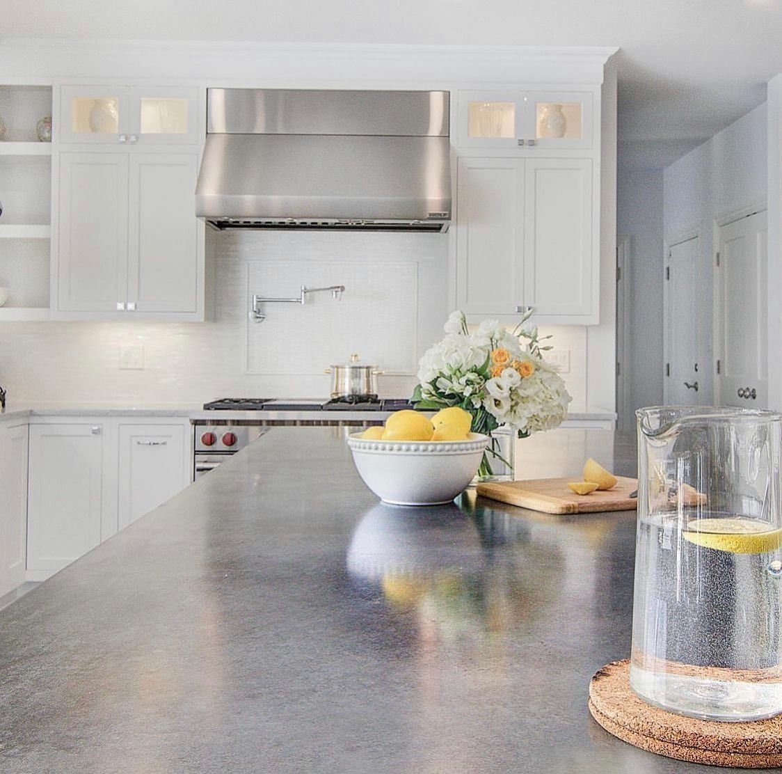 Modern kitchen with white cabinets, stainless steel range hood, dark countertop, and lemons.