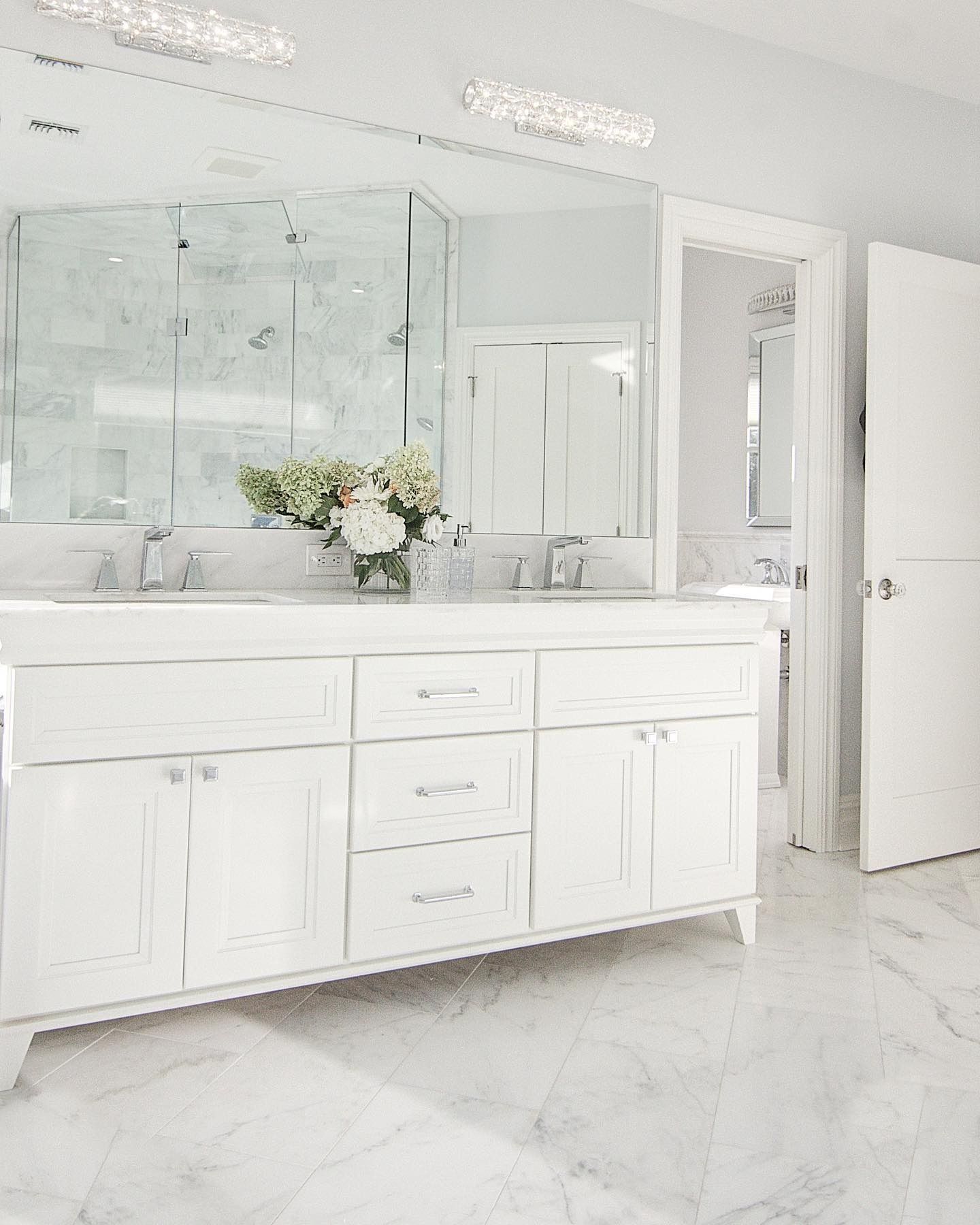 White bathroom with double vanity, marble floor, and large mirror.