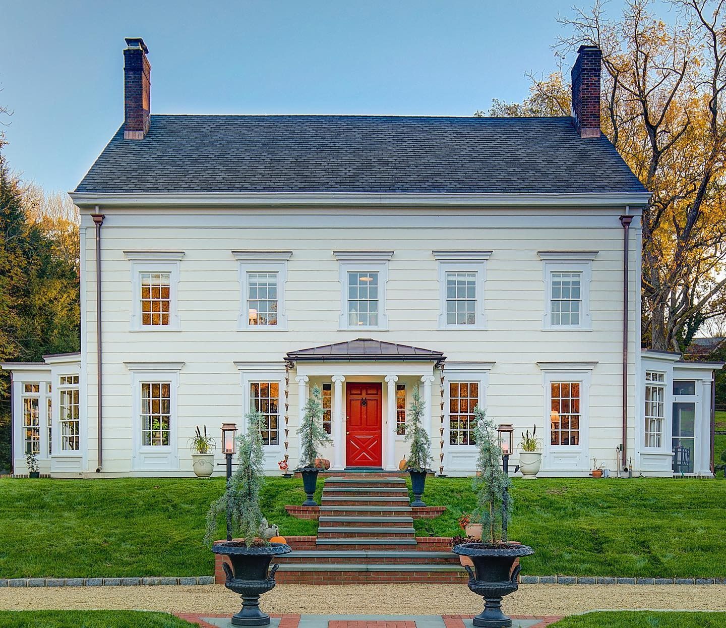White colonial house with red door, symmetrical windows, brick steps, and flanking wings.