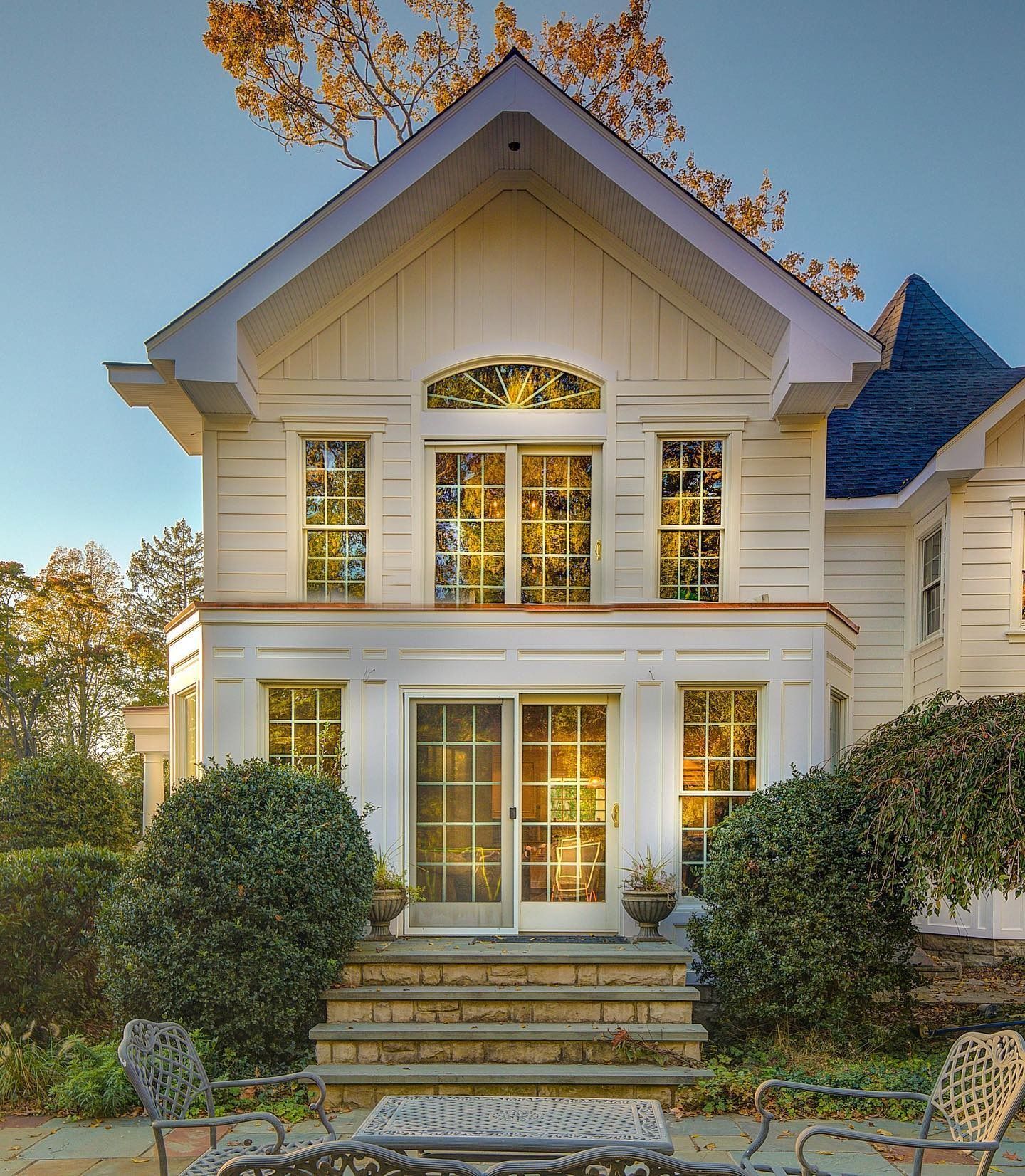 White house with multiple windows, arched top window, and steps. Trees in the background.
