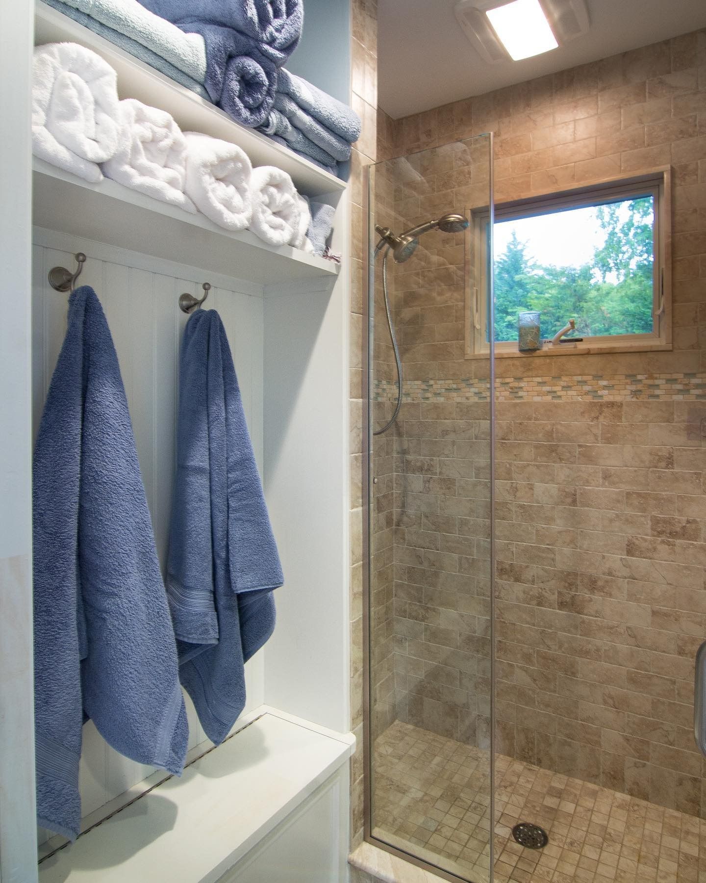 Bathroom with towels on shelves, blue towels hanging on hooks, and a glass shower.