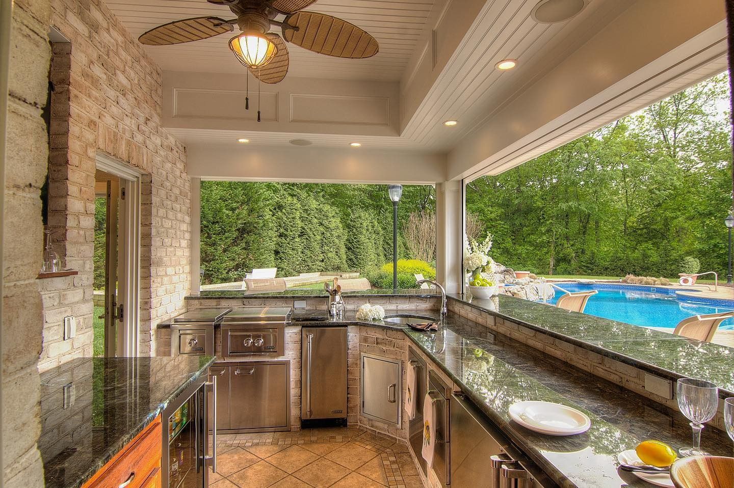 Outdoor kitchen with stainless steel appliances, granite countertops, and a view of a pool.