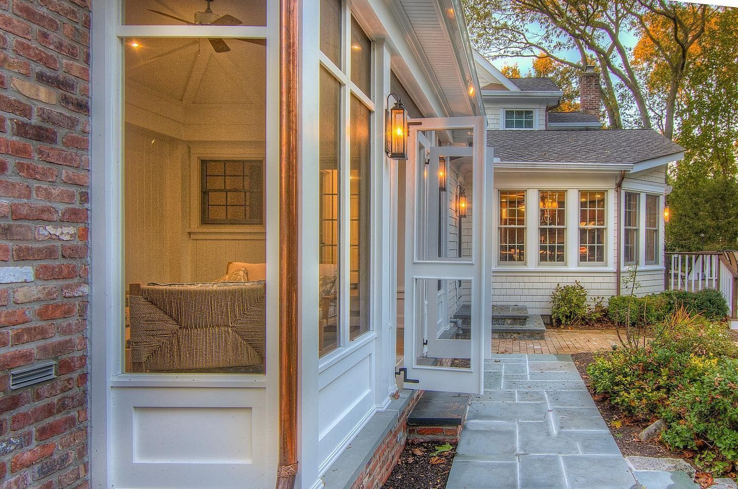White French doors open onto a stone patio from a brick building, view of a house in the background.