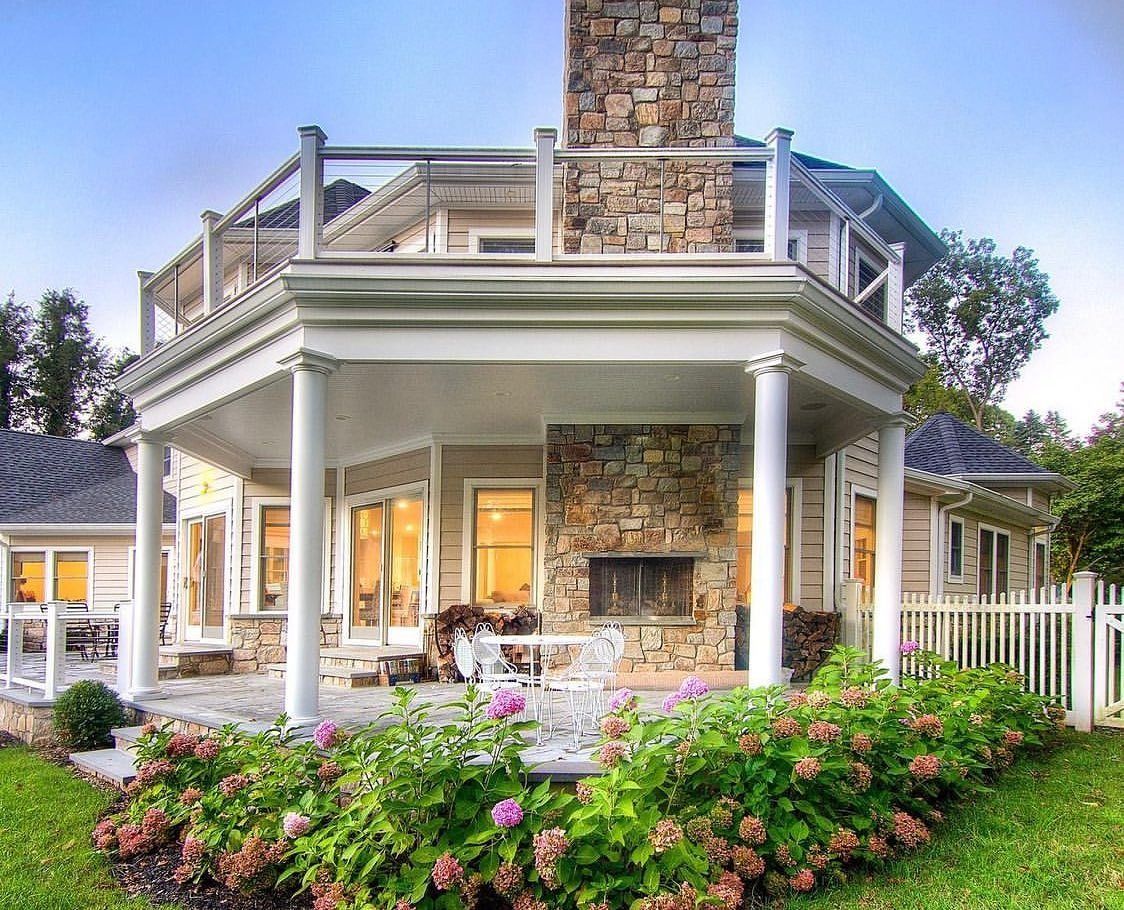 Large house with stone fireplace, outdoor patio, and flowering bushes.