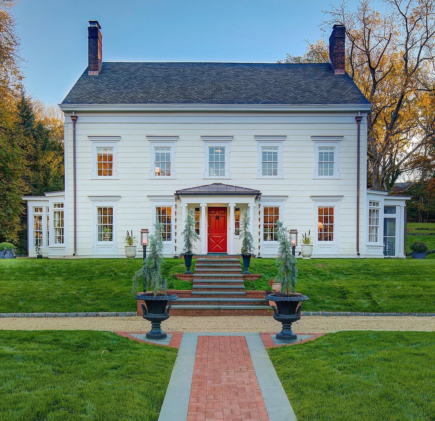 White two-story house with red door, brick path, and green lawn.