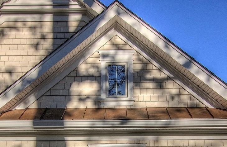 Triangular beige gable with a small window, beneath a clear blue sky.
