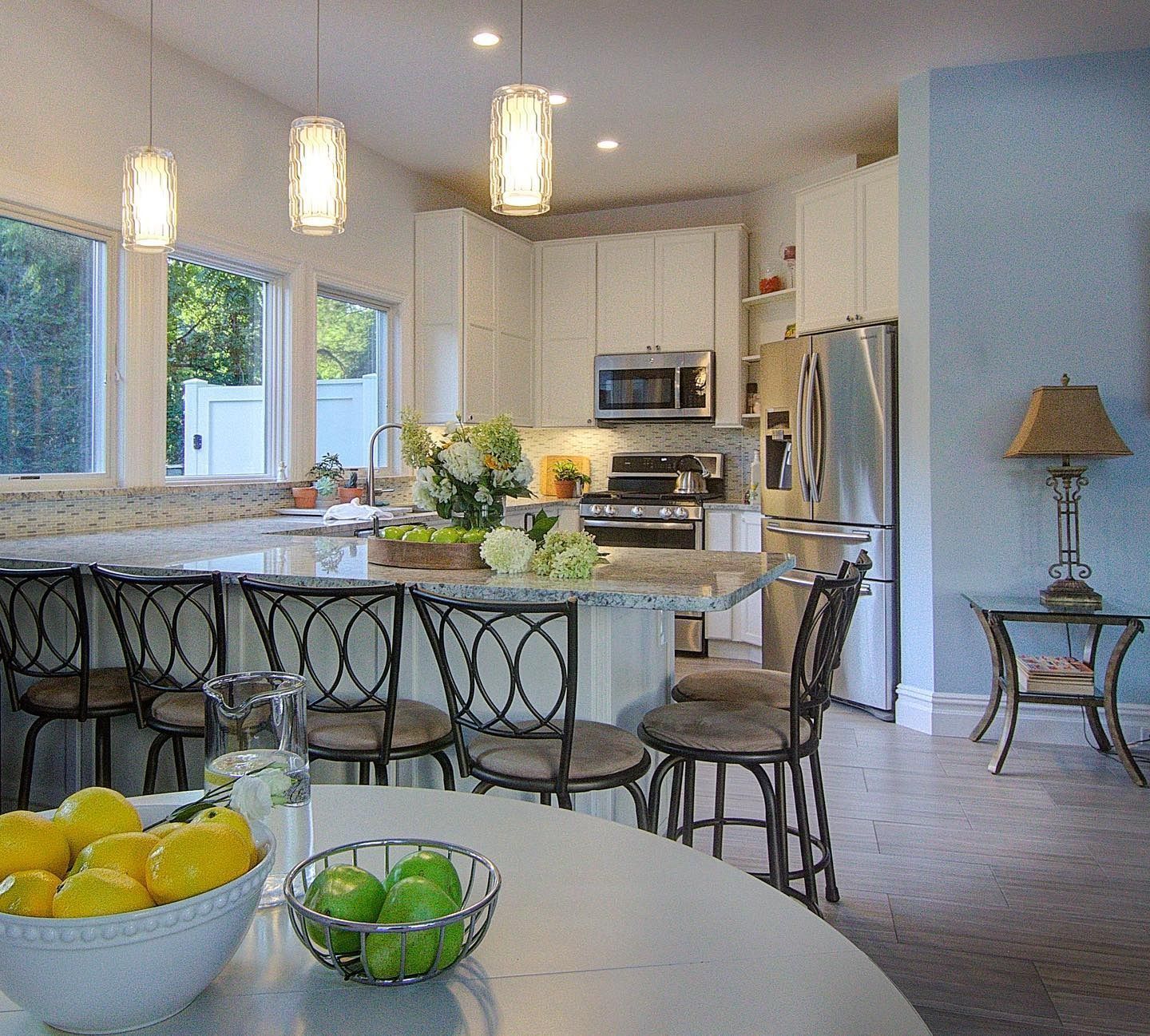Modern kitchen with island, bar stools, pendant lights, stainless steel appliances, and fruit bowl.
