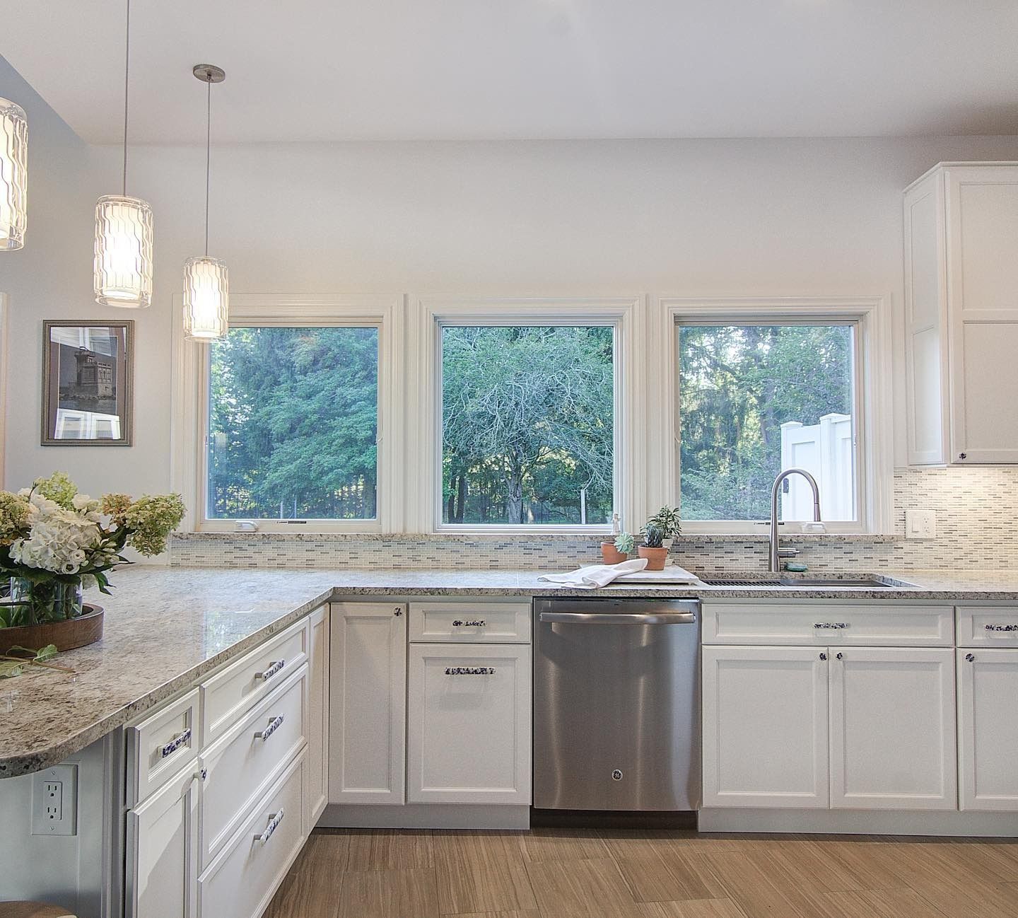 White kitchen with granite countertops, stainless steel appliances, and windows overlooking greenery.