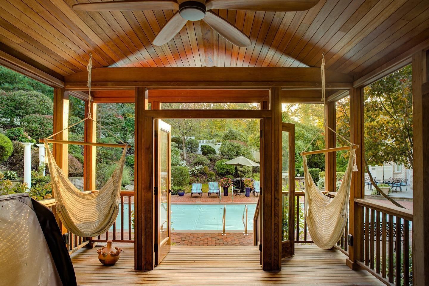 Wooden porch with hammocks overlooking a swimming pool and lush garden.