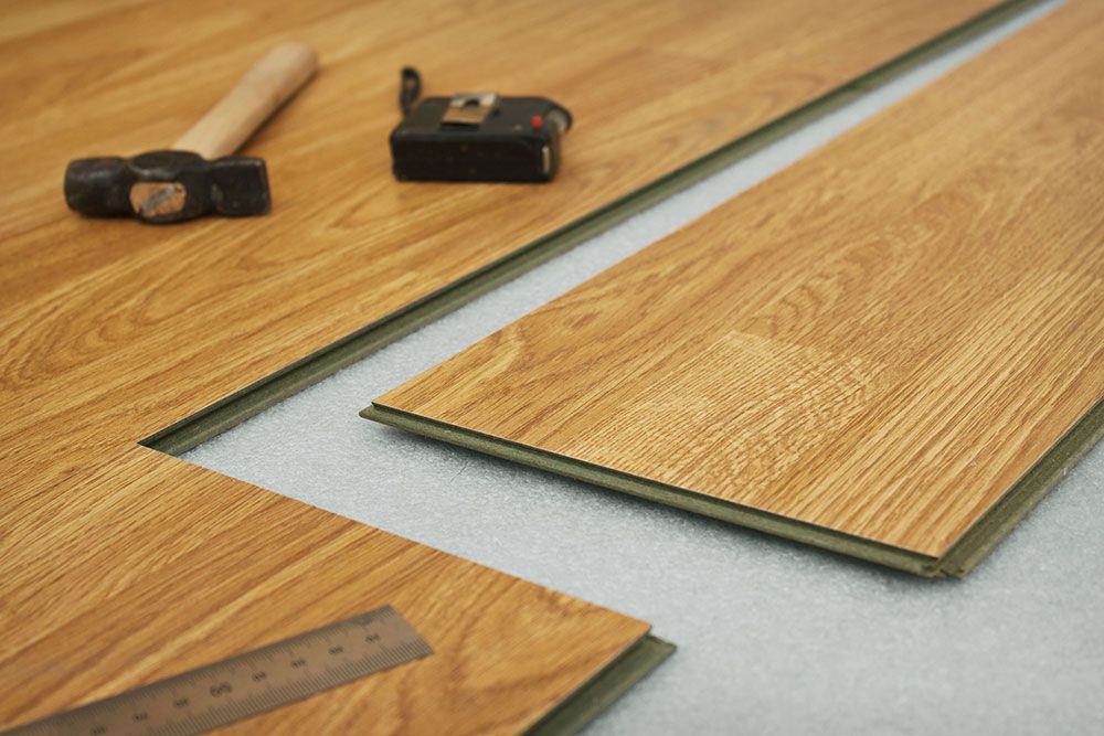 Installing laminate flooring: planks with interlocking edges, hammer, tape measure, and ruler on a white surface.