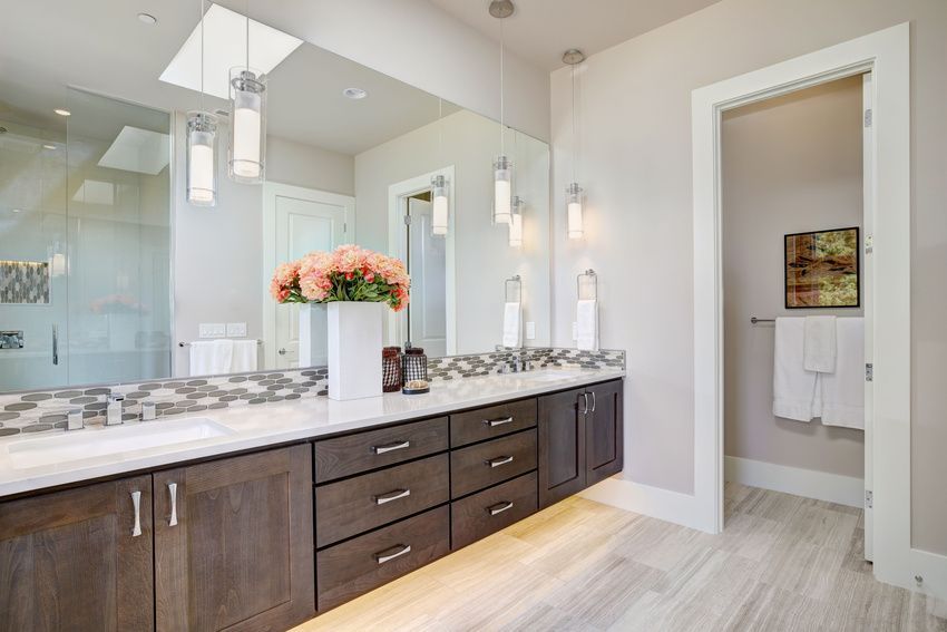 A modern bathroom with a long dark wood vanity, a large mirror, and pendant lights. A door leads to a toilet area.
