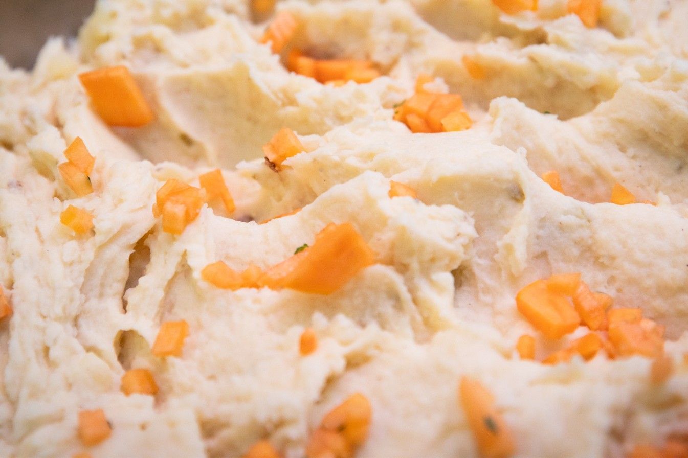 A close up of mashed potatoes with carrots in a bowl.