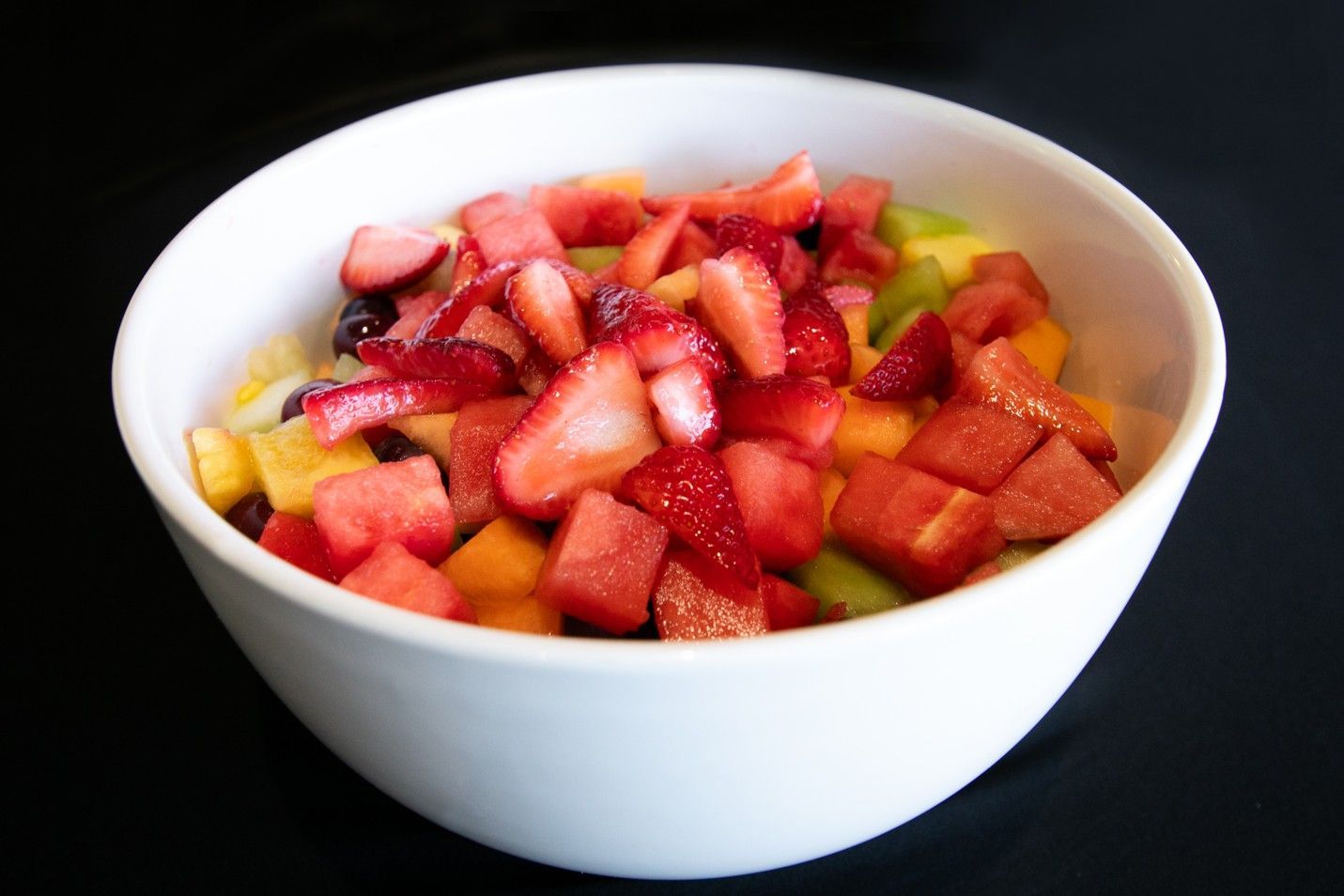 A white bowl filled with sliced fruit including strawberries and watermelon