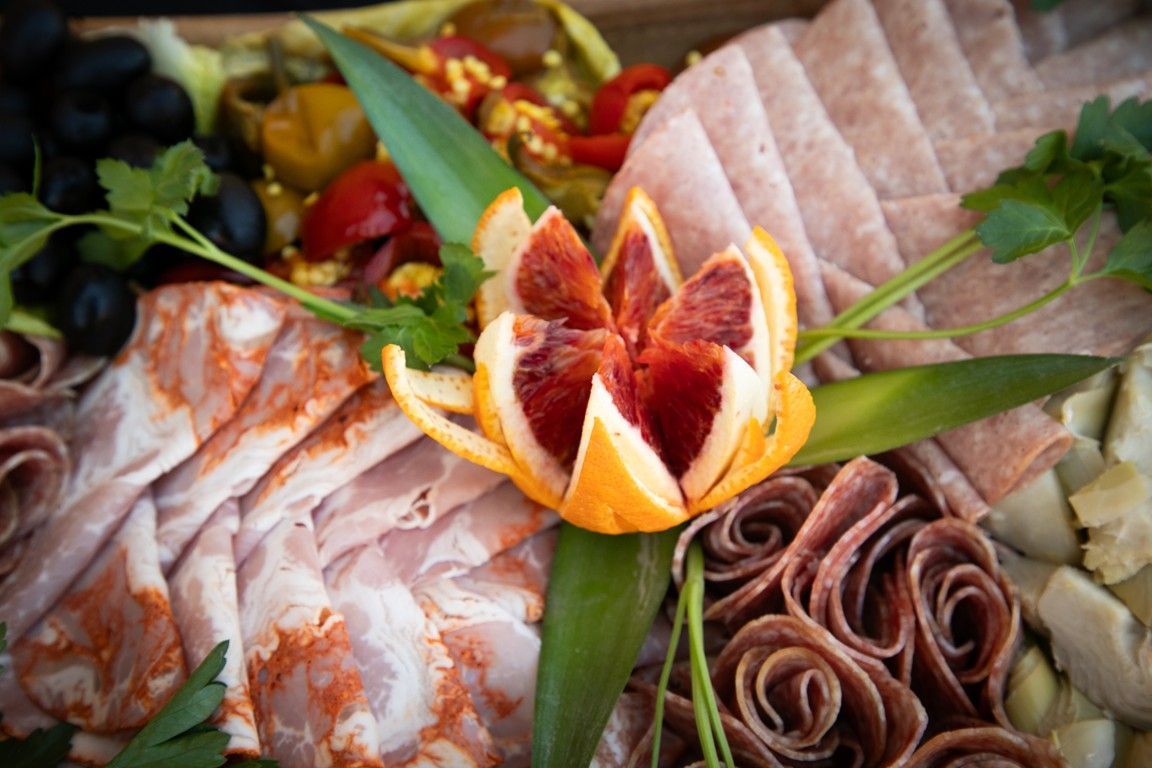A tray of meats and vegetables with a flower made out of orange slices.