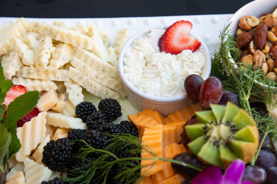 A white plate topped with fruit , cheese , nuts and dip.