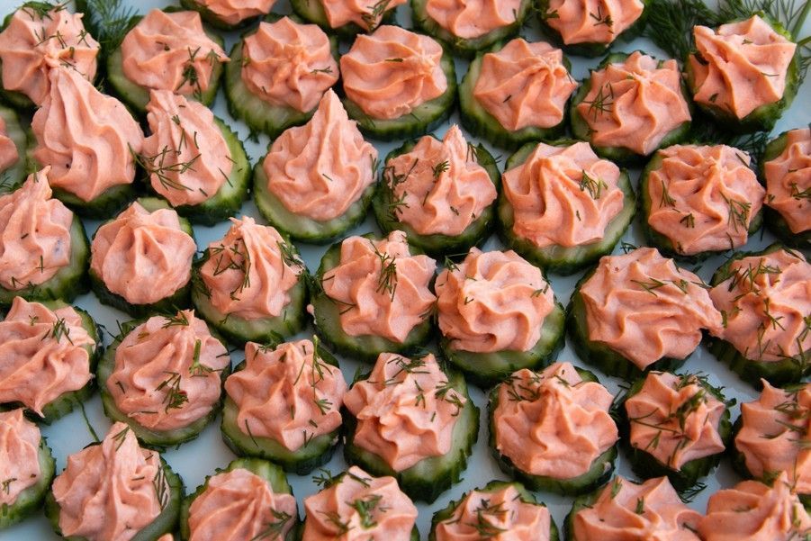 A bunch of cucumber slices covered in pink frosting on a white plate.