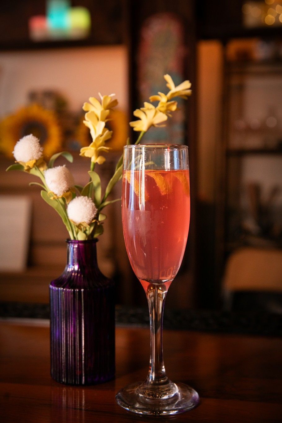 A wine glass filled with a pink drink next to a vase of flowers.