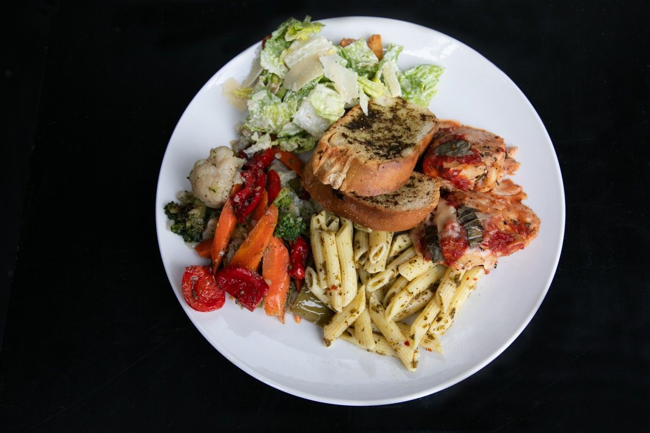 A white plate topped with pasta and vegetables on a black background.