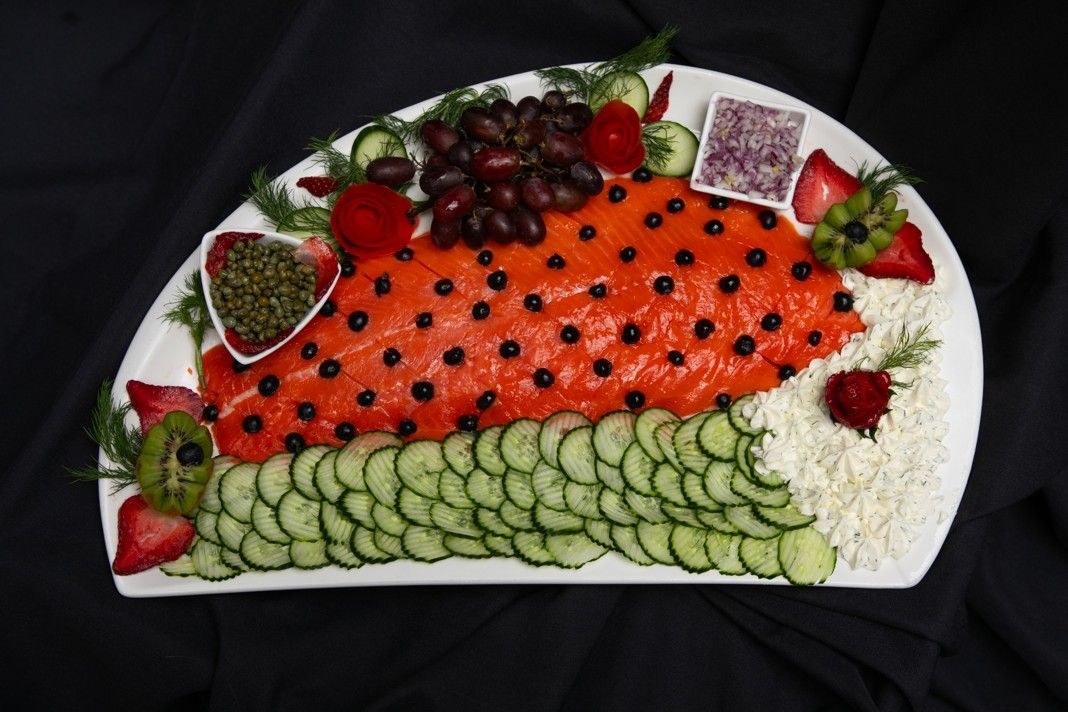 A white plate topped with salmon , cucumbers , grapes and strawberries.