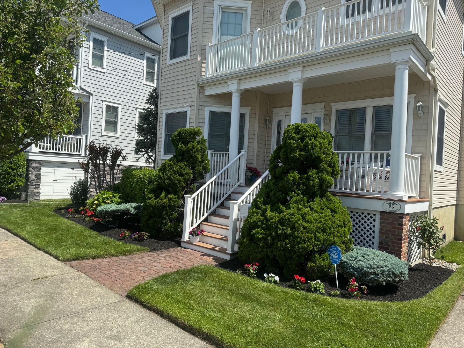 White house with porch and steps, manicured lawn and shrubs on a sunny residential street
