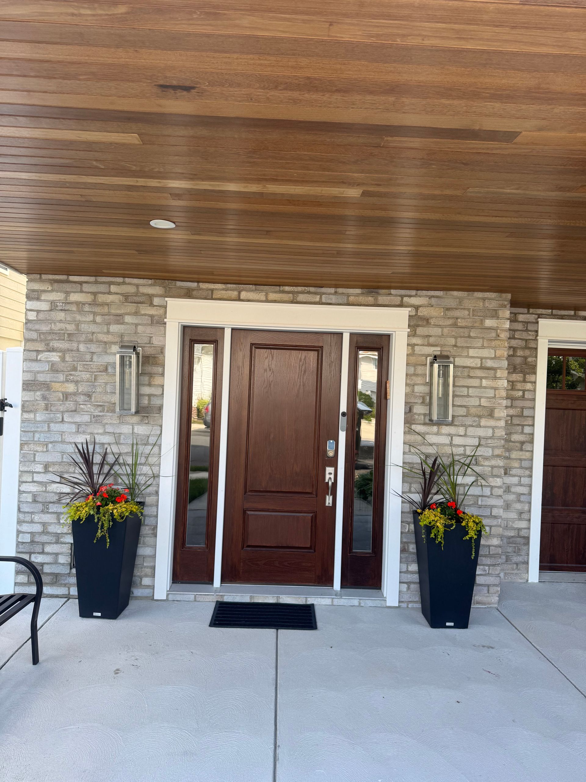 Front entrance with wooden door, stone facade, and two flower planters under a covered porch.