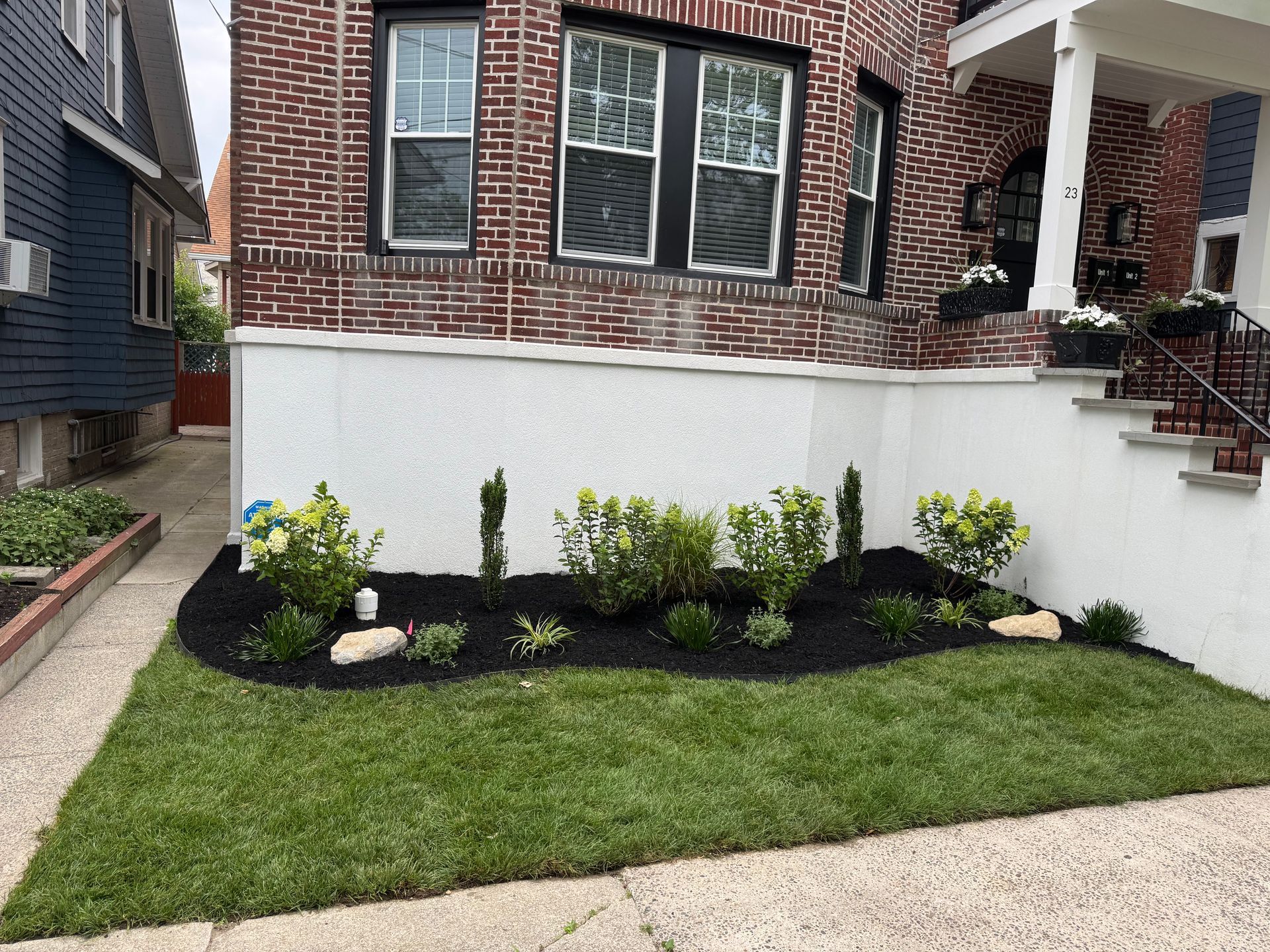 Brick house front yard with fresh landscaping, white retaining wall, and small flower bed along the sidewalk