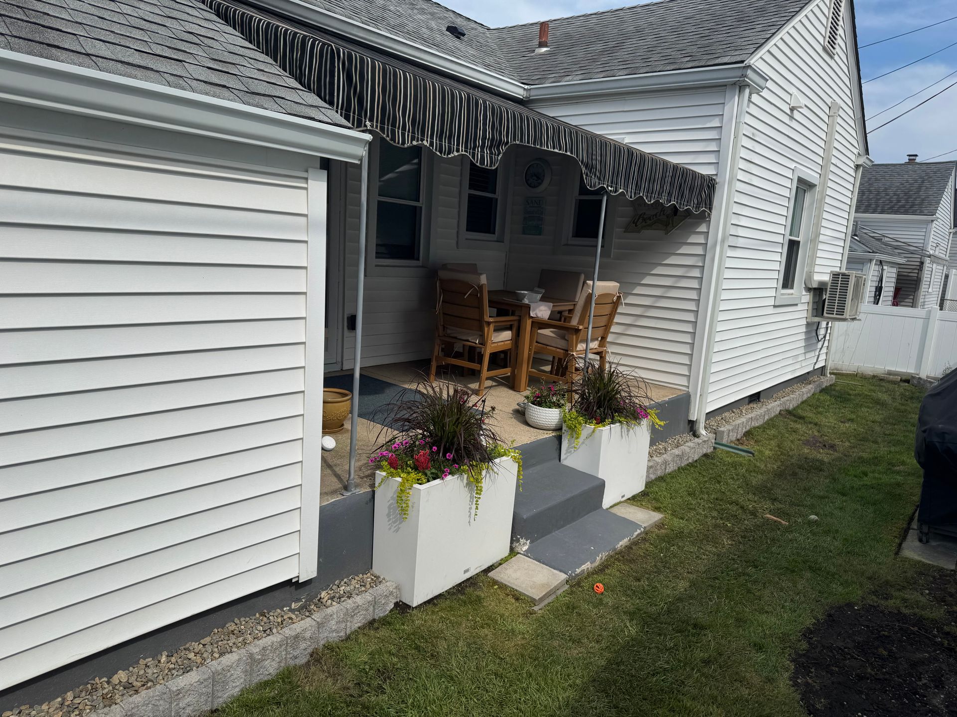 White house porch with chairs and white flower planters along a grassy side yard