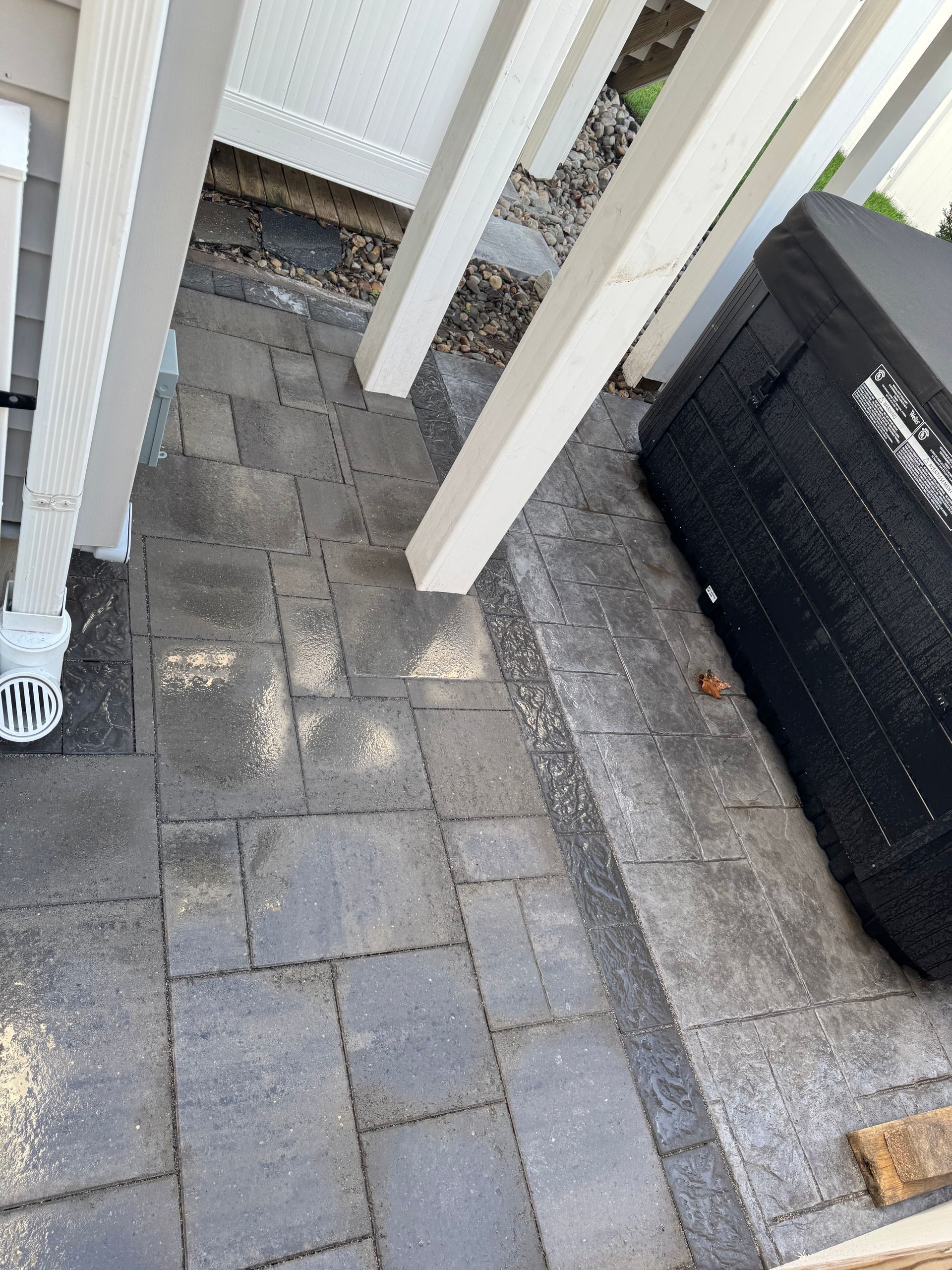 Paved patio with white posts, near a black object, and side of a house.