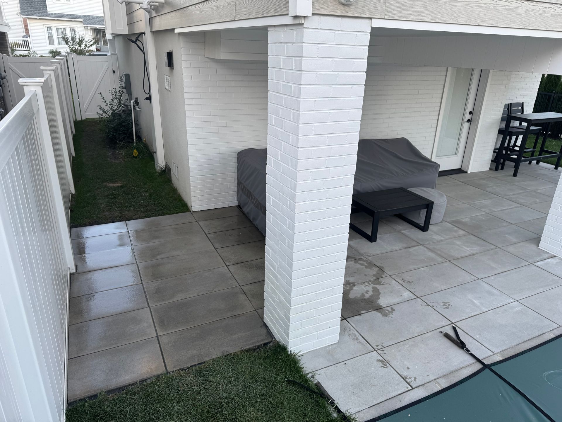 Outdoor patio with concrete tiles, white brick wall, covered furniture, and a fence.