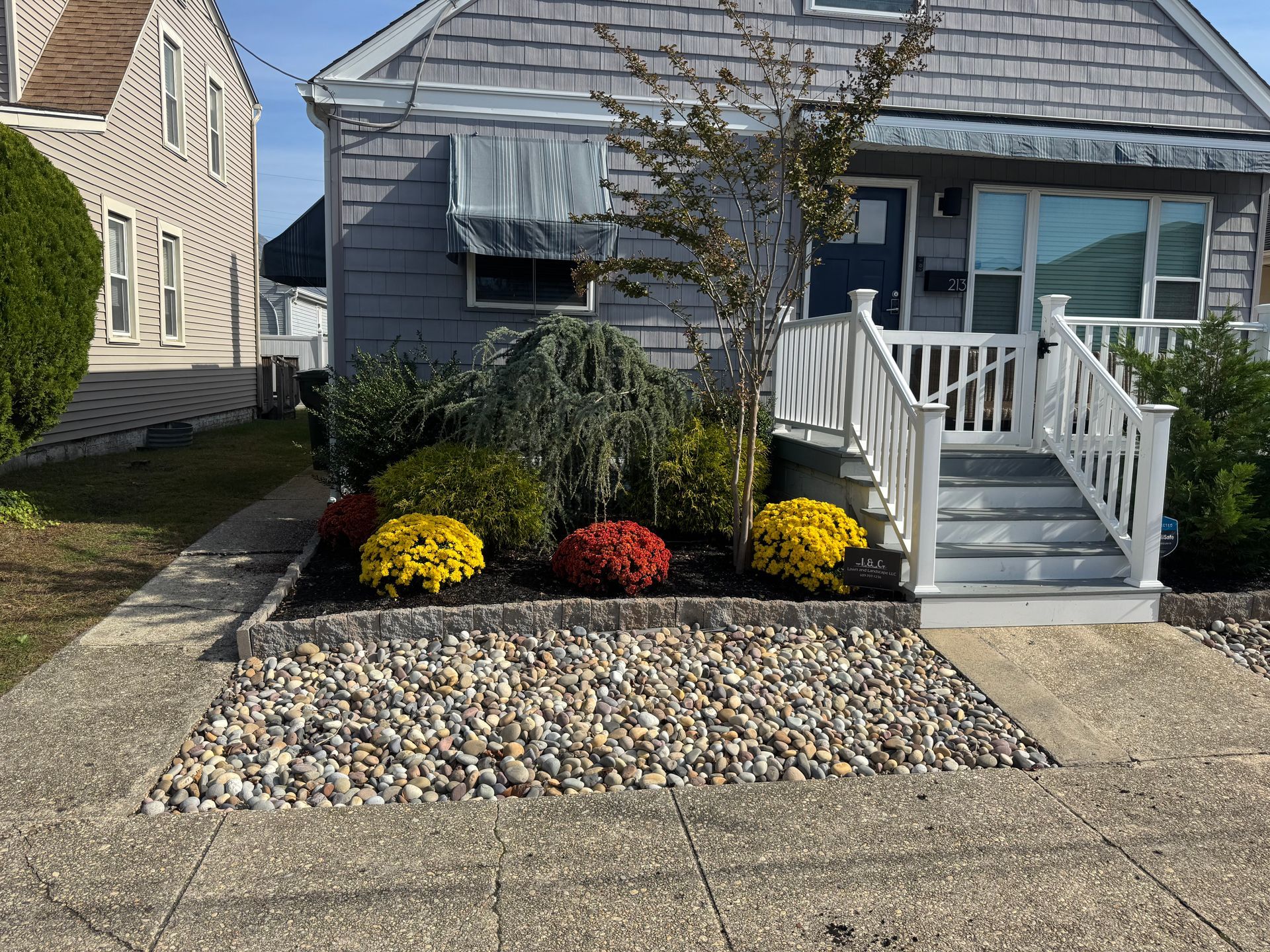 Gray house with a small garden bed filled with colorful mums and river stones.