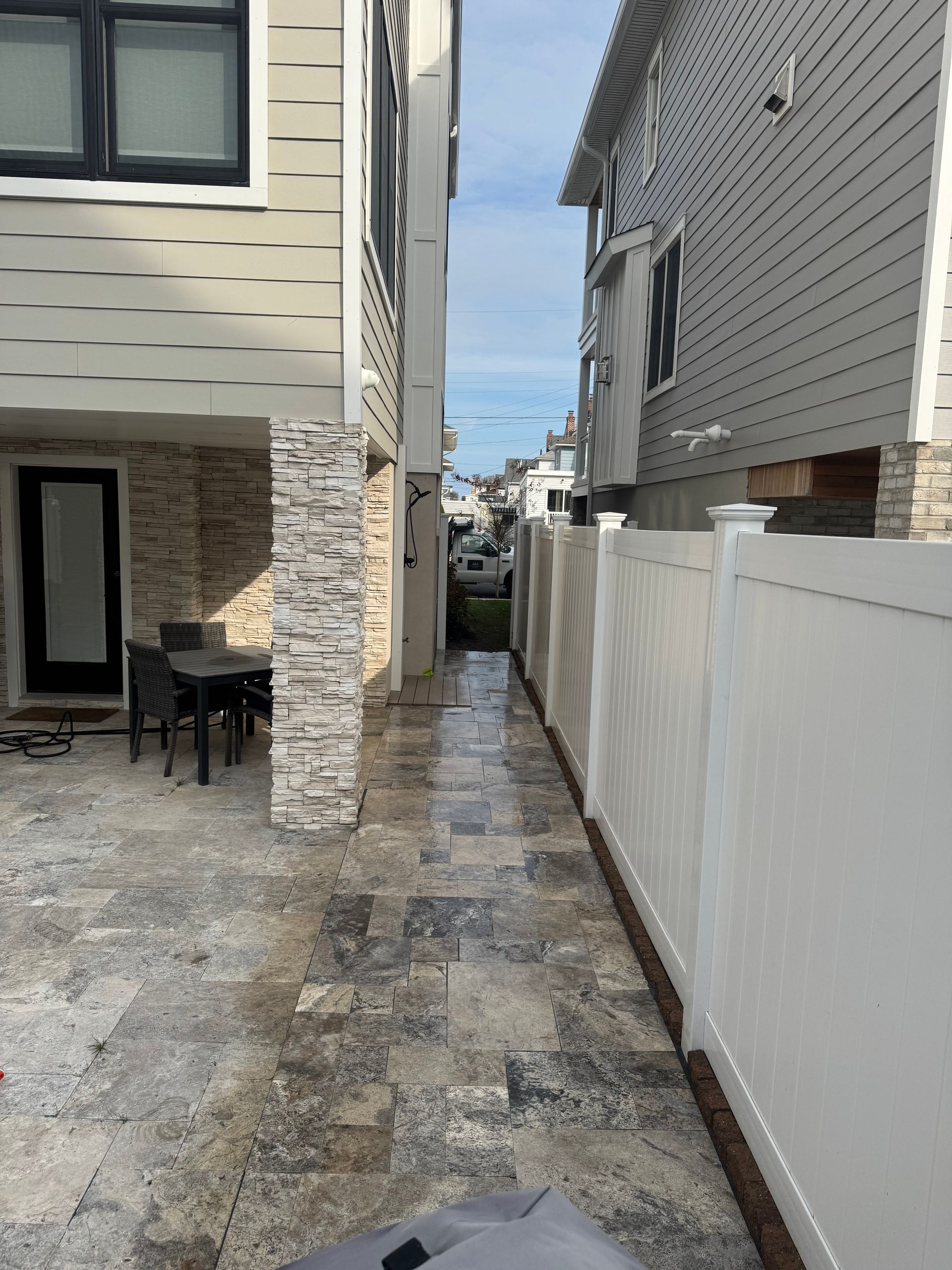 Narrow paved walkway between two buildings with a white fence on the right.