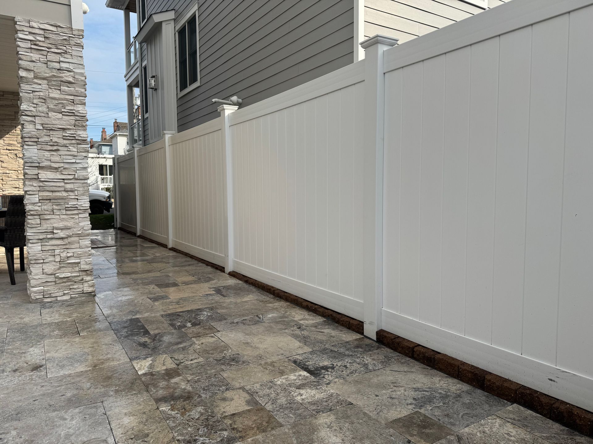 White vinyl fence along a paved patio; adjacent to a building with gray siding.