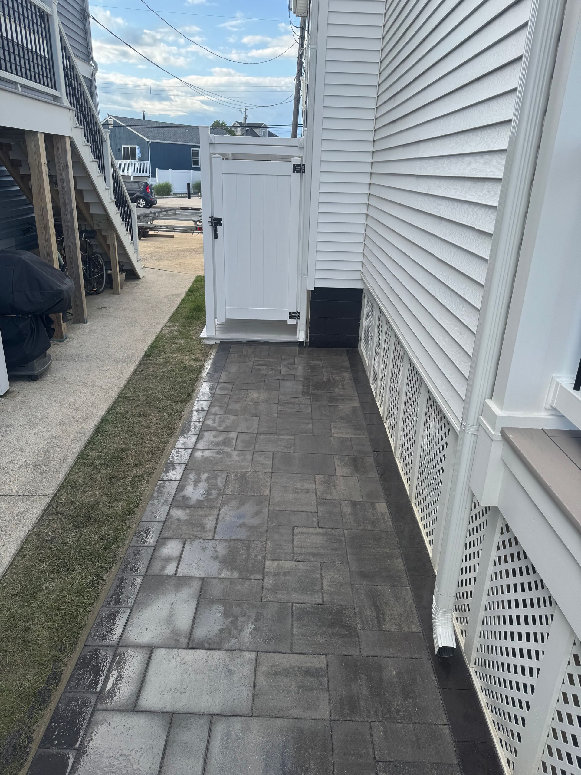 Narrow paved walkway beside a white building and grass. A white door is at the end.