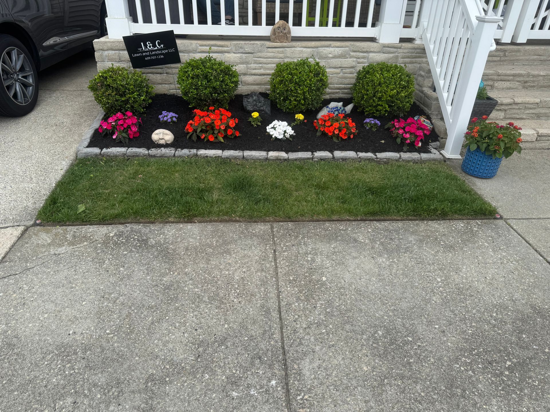 A front yard flower bed with green bushes and colorful flowers.