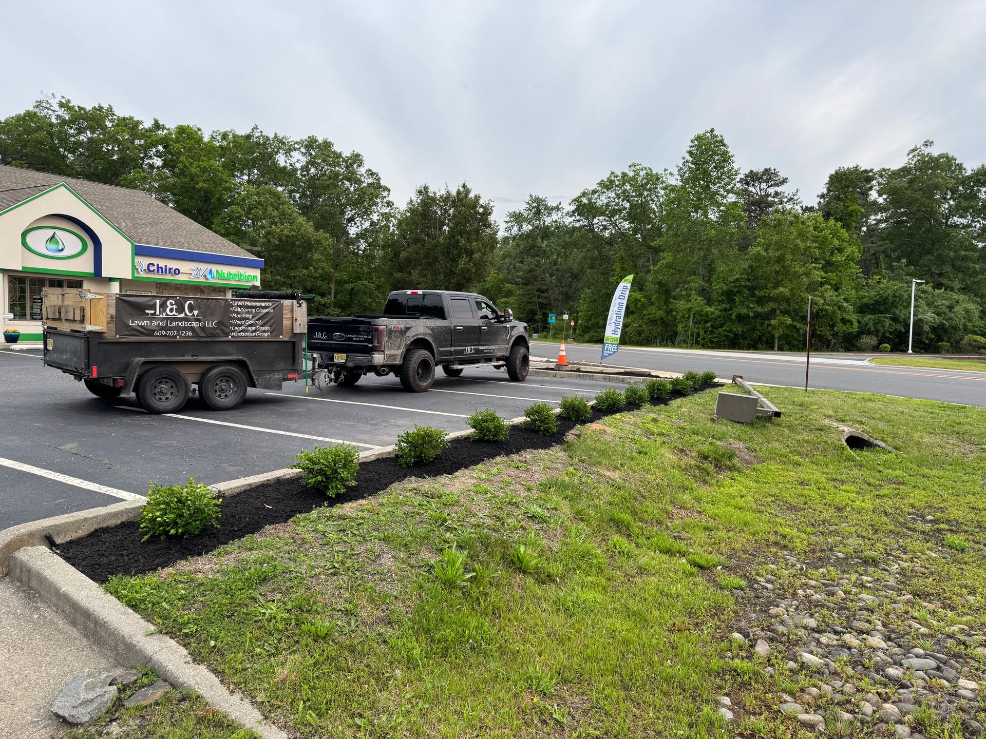 Dark truck with trailer parked outside a store, boxes on trailer, bushes in front.