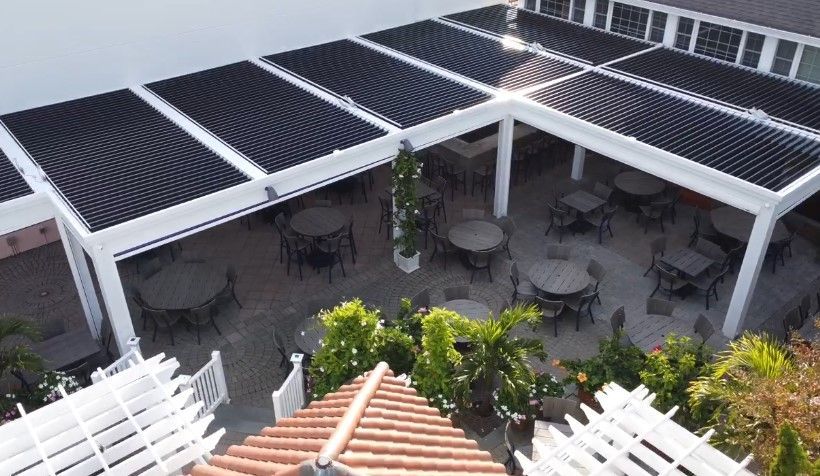 Courtyard patio with tables and chairs under a white pergola and dark canopy roofing