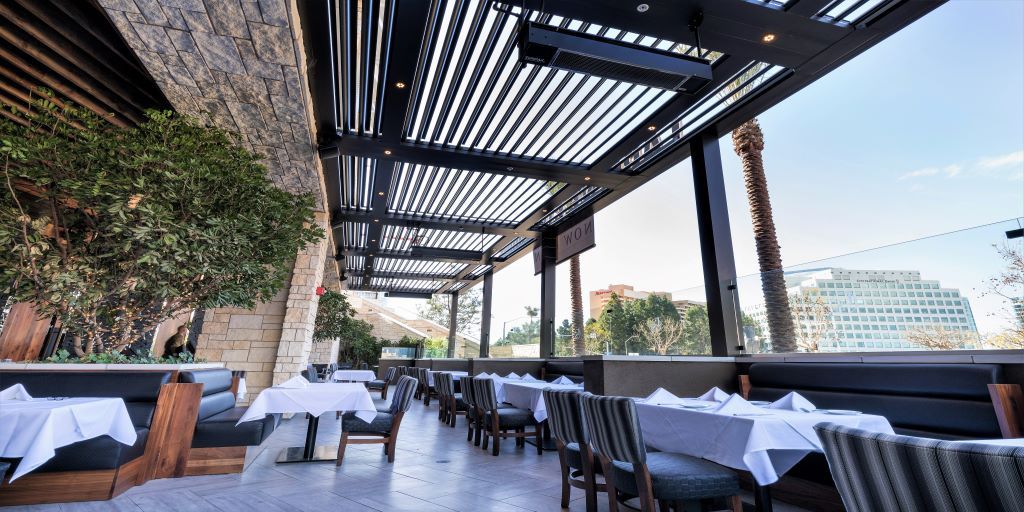 Outdoor rooftop restaurant terrace with white tablecloth tables, pergola shade, and city views