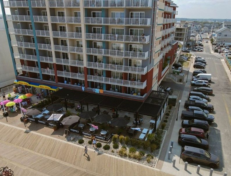 Beachfront hotel with balcony rooms, outdoor café seating, and parked cars along a street