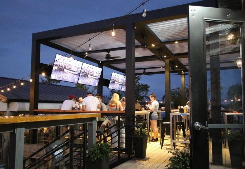 Outdoor rooftop bar with people seated at tables under a lit canopy at dusk