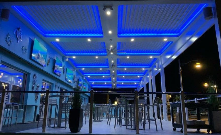 Blue-lit outdoor restaurant patio with tables, chairs, and hanging lights at night